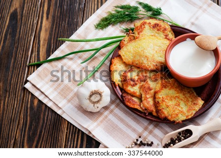potato pancakes with sour cream , herbs , garlic and spices on a wooden background