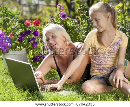 girl\'s granddaughter and her grandmother in garden at leisure with laptop computer