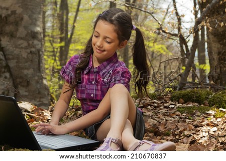 Pretty young girl using laptop in the forest