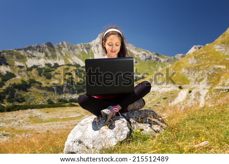 Pretty young girl using a laptop on a rock in the mountains