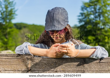 Beautiful young girl with smart phone and headphones listening to music outdoors on sunny spring day.