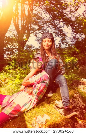 lazy summer day in the woods.Two young girls enjoy relaxed listening to music under the sun. Vintage look vith glow.