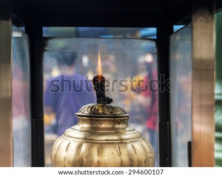 An oil lamp within a glass case has a flickering flame  used for lighting incense sticks at Erawan Shrine in central Bangkok, Thailand
