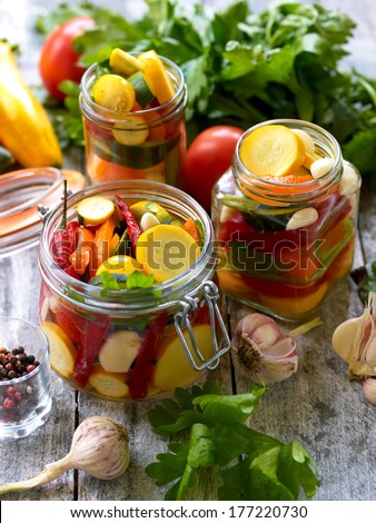 Preparing preserves of pickled zucchini, pepper and tomatoes in jars with spices, garlic and herbs with selective focus