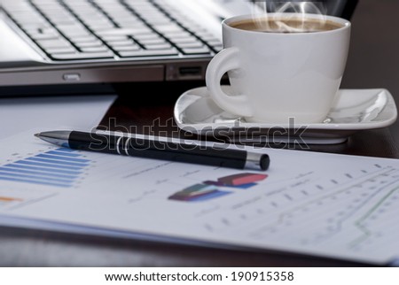 White cup of hot coffee and computer or laptop and paper and pen on wood table