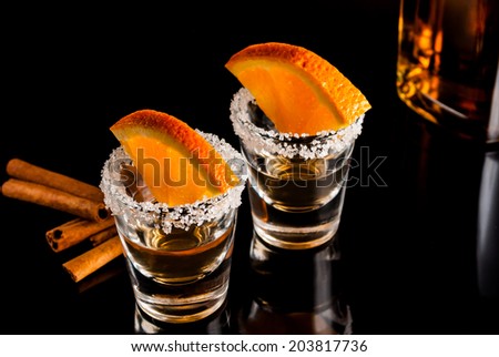 Gold tequila with orange and cinnamon on black reflect background