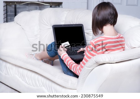 young girl on a white sofa with a laptop and credit card