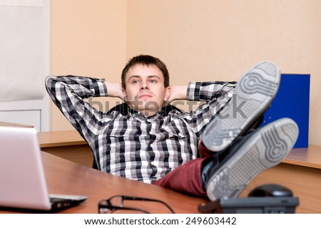 Office worker. Young office worker resting his feet on the table
