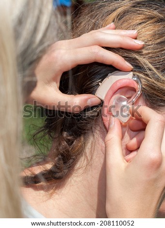 Woman helping in inserting a hearing aid for a hearing impaired woman in outdoor