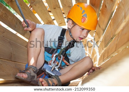 Cute boy with climbing equipment in an adventure park in a wooden tunnel