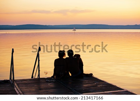 Romantic scene - Young couple sitting on a pier at a lake after sunset
