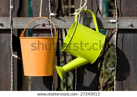 A metal watering can and bucket hanging from a wood fence.