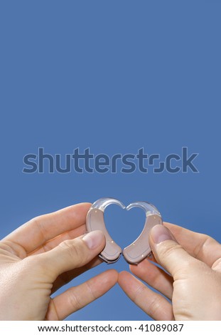 Hands forming a heart shape from digital hearing aids in front of a blue sky background useful for texts.