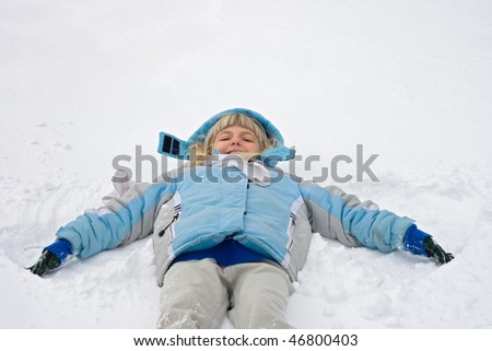 Young girl wearing blue coat making a snow-angel.