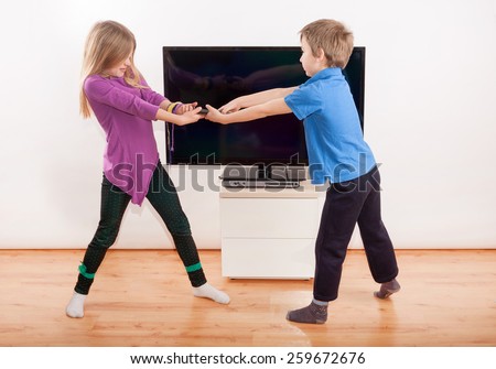 Sibling fighting over the remote control in front of the TV