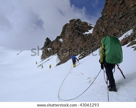 Roped team of mountaineers approaching a mountain pass.