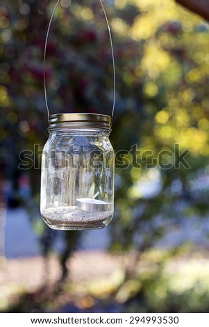 Mason jar candle lantern hanging from tree used as decoration for parties, weddings and celebrations.