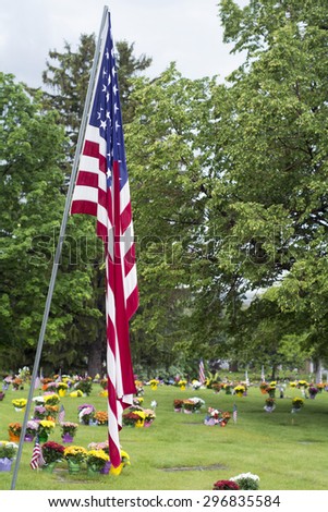 Flag on Memorial Day with flowers and graves in background.