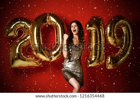 New Year. Woman With Balloons Celebrating At Party. Portrait Of Beautiful Smiling  excited Laughing Girl In Shiny Golden Dress Under Snow Confetti Having Fun With Gold 2019 Balloons On Red Background