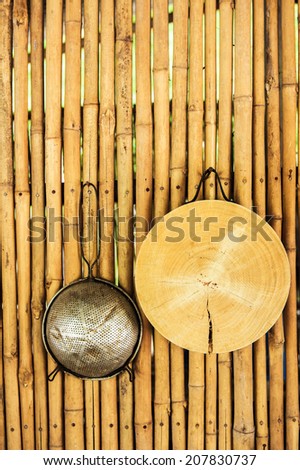 Strainer and wooden cutting board hanging on a bamboo wall in an outdoor kitchen