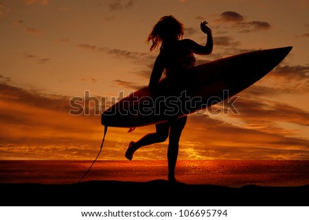 A silhouette of a woman holding on to her surf board running on the beach.