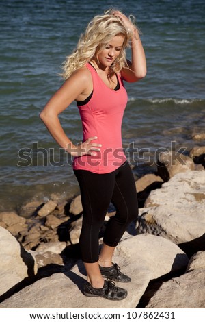 A woman in a pink tank top is standing by the water looking down.