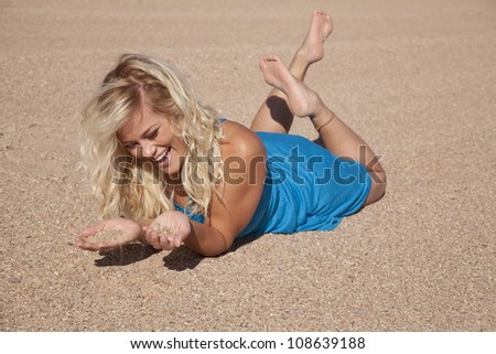 A woman laying in the sand with her feet up laughing and placing sand in her hands.