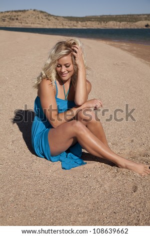 A woman sitting on the beach looking down at the sand with her hand in her hair.
