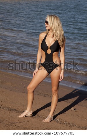 a woman standing on the beach looking away with her sunglasses on.