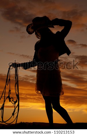a cowgirl holding onto her bridle with a beautiful sunset in the background.