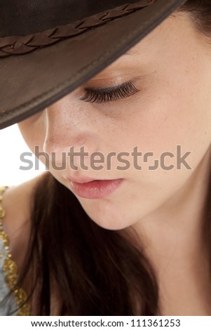 A close up of a woman\'s face looking down with a cowgirl hat on.