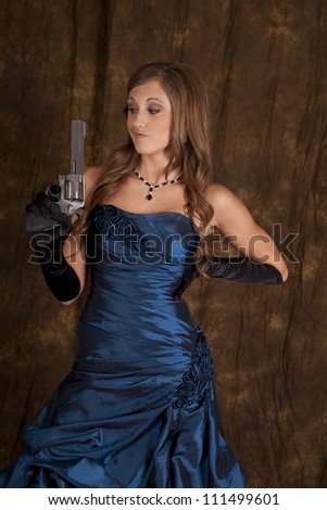 A teen girl in her formal dress holding a pistol with a funny expression on her face.