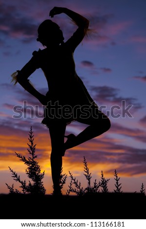A silhouette of a woman dancing with a colorful sky behind her.