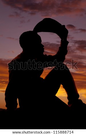 a silhouette of a cowboy sitting and holding his hat thinking