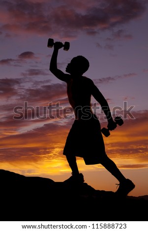 A silhouette of a man climbing up a hill working out with weights.