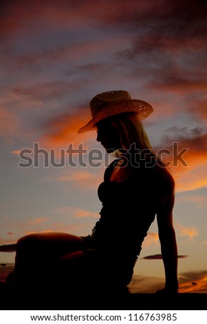 A cowgirl is sitting in the sunset as a silhouette.