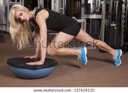 A woman on a half of a ball in plank position bringing in her knee.