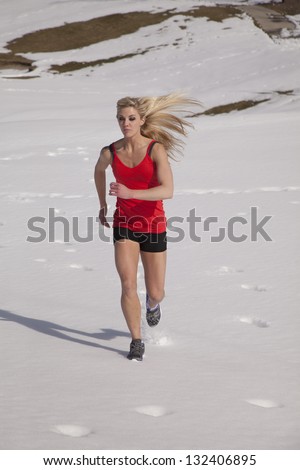 A woman running in the snow in her shorts and tank in the snow.