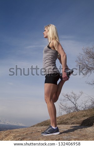 A woman lifting up her leg to stretch in the outdoors.