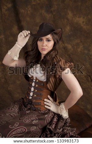 A woman with a serious expression sitting in her vintage western dress and hat.