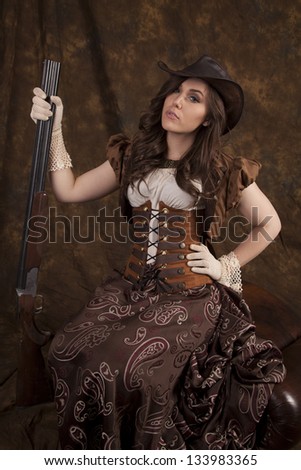 a woman in her vintage western dress holding on to a shotgun with a serious expression on her face.