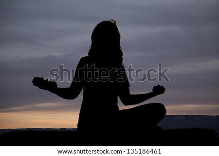 A silhouette of a woman sitting and working out with weights.