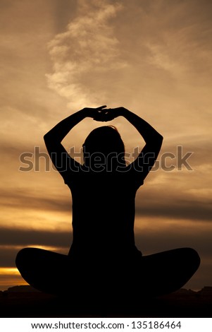 A silhouette of a woman sitting and doing a yoga stretch.