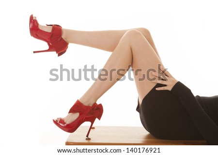 A woman laying on a bench with her red heels kicked up