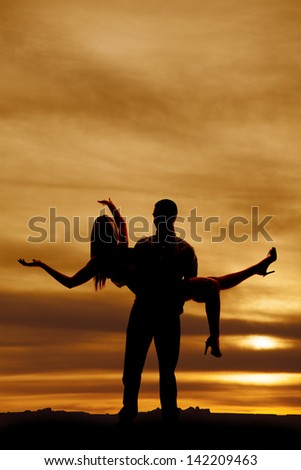 a silhouette of man holding on to a woman while she throws her arms out