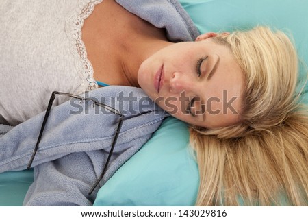 A woman laying down asleep with her glasses on her shoulder.