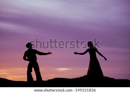 A cowboy is reaching back for a woman in the sunset.