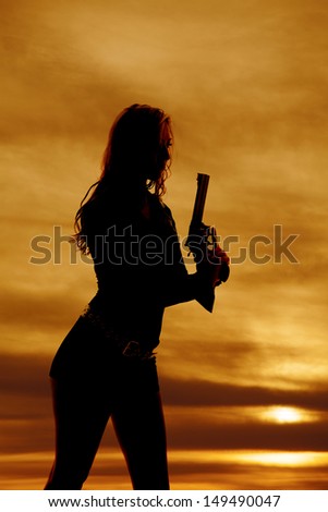 A woman is holding up a gun in the sunset silhouetted.