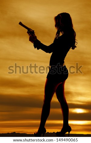 A woman silhouette in the sunset profile holding a gun.