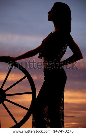 A woman standing by a wagon wheel silhouette night sky.